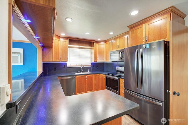 kitchen featuring dark countertops, recessed lighting, appliances with stainless steel finishes, a sink, and a peninsula