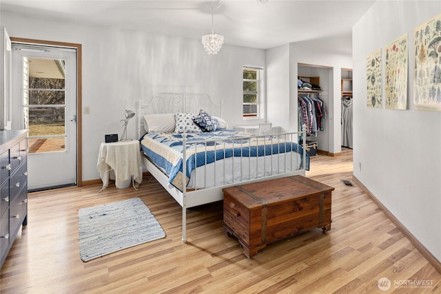 bedroom featuring visible vents, baseboards, light wood-style flooring, a walk in closet, and a notable chandelier