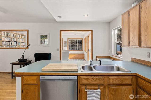 kitchen with light countertops, stainless steel dishwasher, light wood-style floors, a sink, and a peninsula