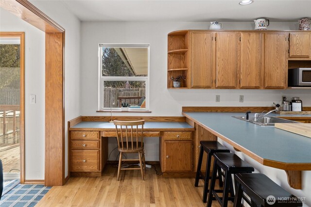 kitchen with stainless steel microwave, a sink, light wood-type flooring, built in study area, and brown cabinetry