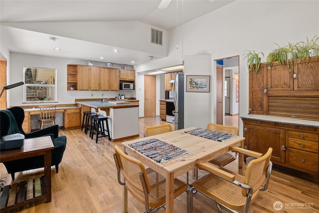 kitchen featuring light wood finished floors, open shelves, stainless steel microwave, visible vents, and brown cabinetry