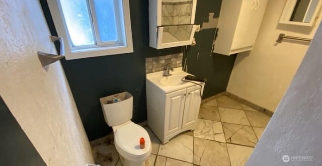 bathroom with baseboards, vanity, toilet, and decorative backsplash