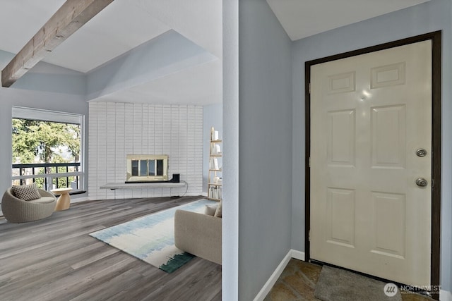 interior space featuring a brick fireplace, beamed ceiling, baseboards, and wood finished floors