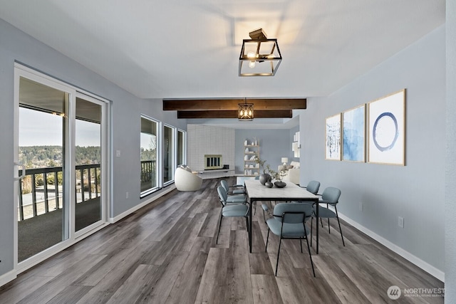 dining room with beam ceiling, baseboards, a fireplace, and wood finished floors