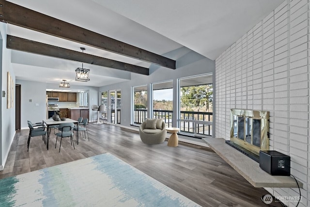 living area with a brick fireplace, beamed ceiling, baseboards, and wood finished floors