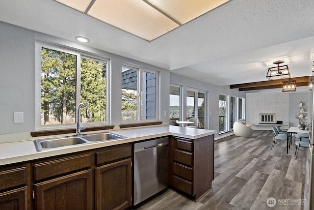 kitchen featuring open floor plan, a peninsula, light countertops, stainless steel dishwasher, and a sink