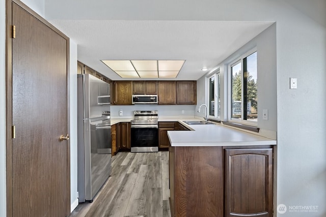 kitchen with stainless steel appliances, light countertops, light wood-style flooring, a sink, and a peninsula