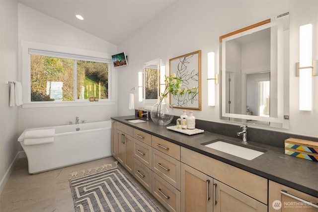 full bath featuring lofted ceiling, double vanity, a soaking tub, and a sink