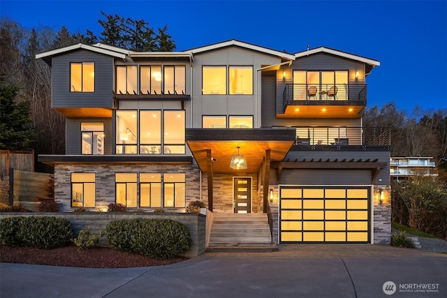 contemporary home featuring a balcony, stone siding, driveway, and an attached garage