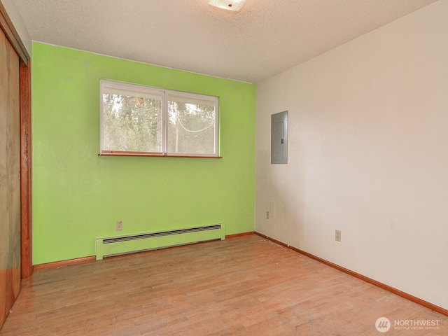 empty room with a baseboard heating unit, a textured ceiling, wood finished floors, electric panel, and baseboards