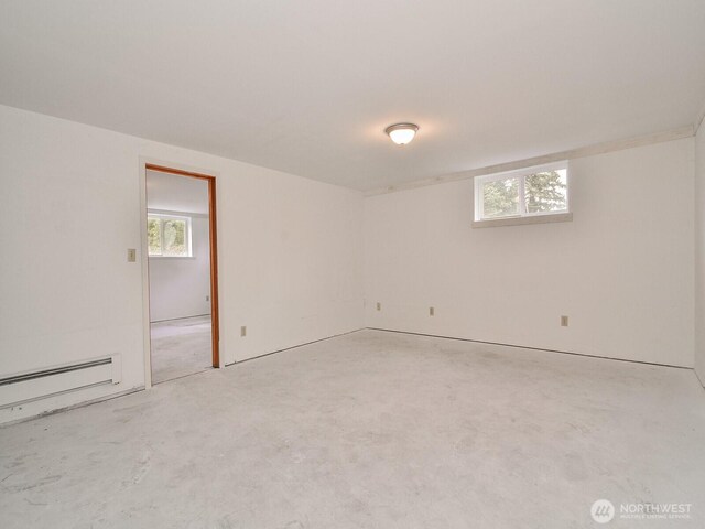 empty room featuring a healthy amount of sunlight, unfinished concrete floors, and a baseboard heating unit