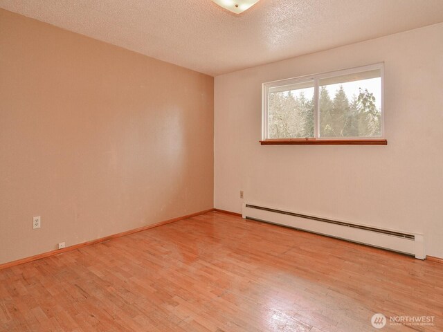 unfurnished room with a baseboard heating unit, a textured ceiling, baseboards, and wood finished floors