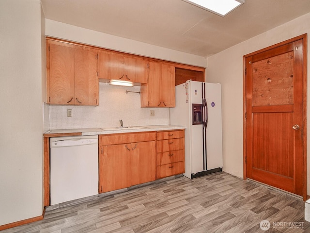 kitchen with light wood-type flooring, white appliances, light countertops, and a sink