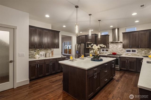 kitchen featuring dark brown cabinets, stainless steel appliances, light countertops, and wall chimney range hood