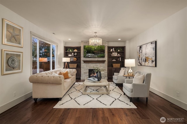 living room with a notable chandelier, built in features, wood finished floors, a stone fireplace, and baseboards