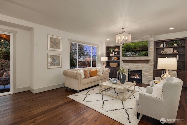 living room with built in shelves, baseboards, a chandelier, a stone fireplace, and wood finished floors