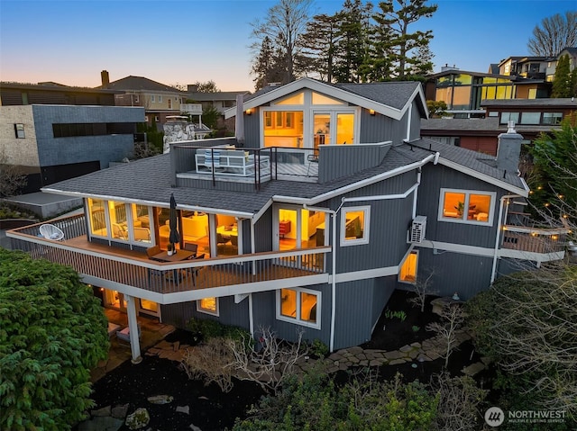 back of property at dusk featuring a balcony and roof with shingles