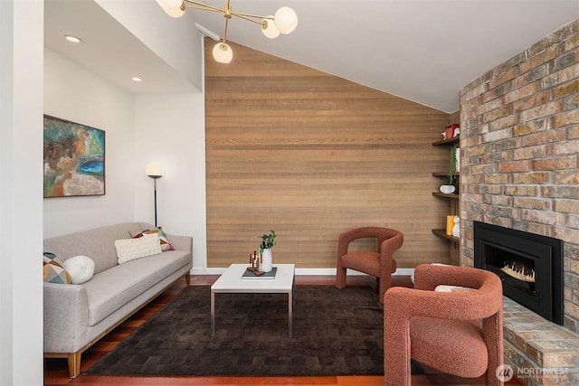 living room with wooden walls, a brick fireplace, baseboards, and vaulted ceiling