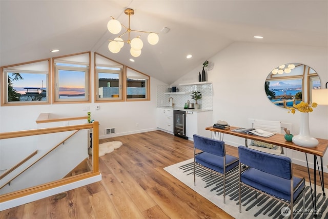 interior space with beverage cooler, visible vents, light wood-style flooring, vaulted ceiling, and indoor bar