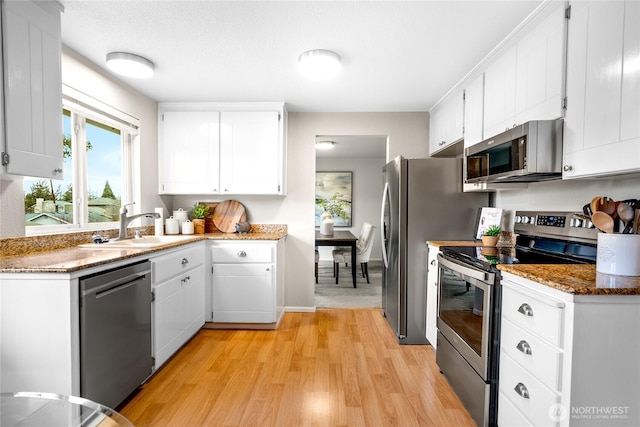 kitchen with stone counters, light wood finished floors, stainless steel appliances, white cabinets, and a sink