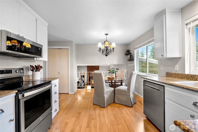 kitchen with a notable chandelier, appliances with stainless steel finishes, white cabinets, and light wood-style floors