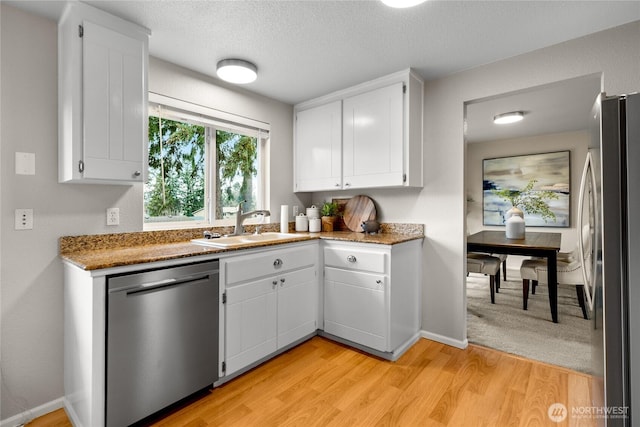 kitchen with light wood finished floors, white cabinets, light stone counters, appliances with stainless steel finishes, and a sink