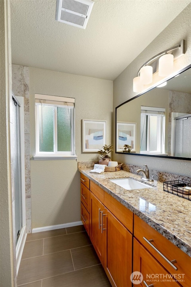 full bath featuring a sink, visible vents, a wealth of natural light, double vanity, and a stall shower