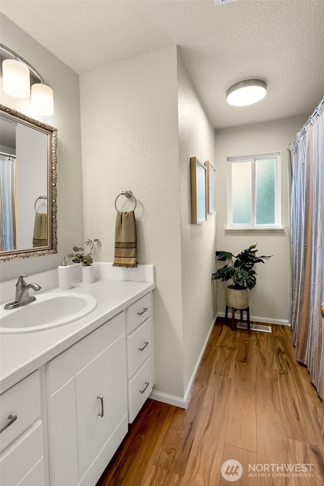 full bathroom featuring a textured ceiling, wood finished floors, vanity, visible vents, and baseboards