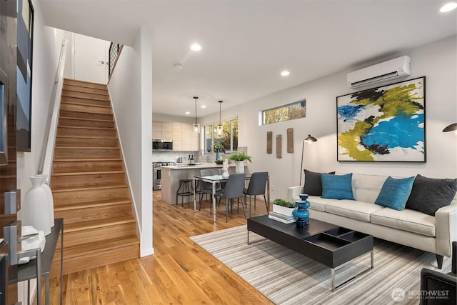 living area with a wall unit AC, recessed lighting, light wood-style flooring, stairway, and baseboards