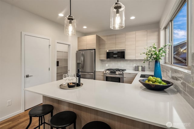 kitchen with stainless steel appliances, wood finished floors, light countertops, decorative backsplash, and a kitchen bar