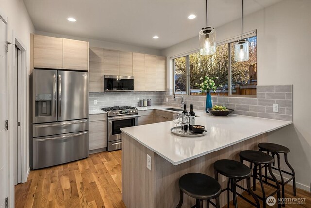 kitchen featuring light wood finished floors, appliances with stainless steel finishes, a kitchen breakfast bar, a peninsula, and a sink