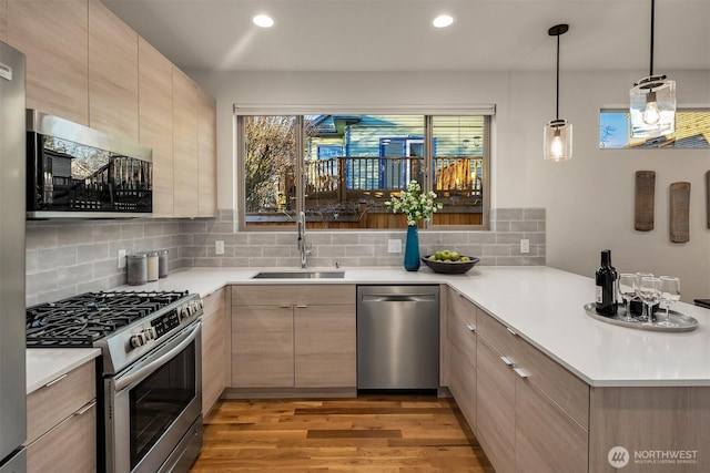 kitchen featuring a peninsula, a sink, appliances with stainless steel finishes, light wood finished floors, and modern cabinets