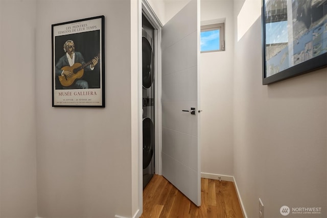 hall featuring baseboards, wood finished floors, and stacked washer and clothes dryer