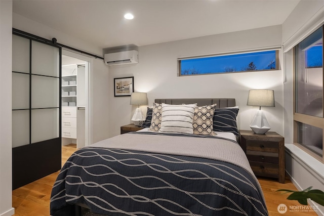 bedroom with a barn door, recessed lighting, wood finished floors, a wall mounted air conditioner, and ensuite bath