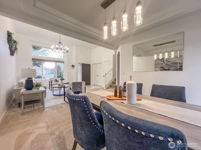 dining space with a notable chandelier, light carpet, baseboards, stairs, and a raised ceiling