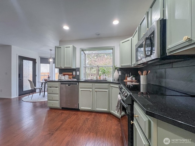 kitchen with appliances with stainless steel finishes, a sink, dark wood finished floors, and decorative backsplash