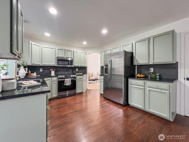 kitchen featuring arched walkways, dark countertops, dark wood-style floors, stainless steel appliances, and backsplash