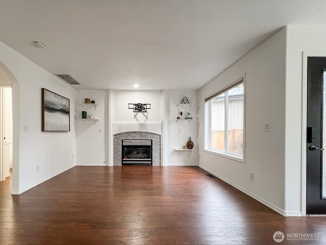 unfurnished living room with arched walkways, a glass covered fireplace, dark wood finished floors, and visible vents