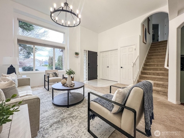 living area featuring light carpet, baseboards, a towering ceiling, stairway, and an inviting chandelier