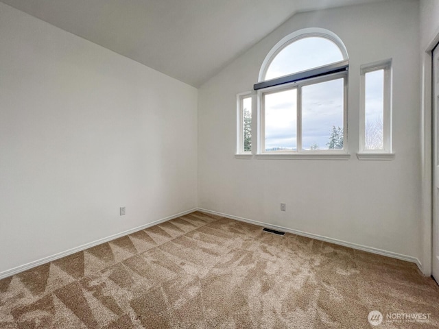 carpeted spare room with baseboards, visible vents, and vaulted ceiling