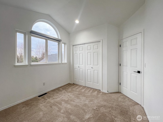 unfurnished bedroom with carpet, visible vents, vaulted ceiling, and baseboards