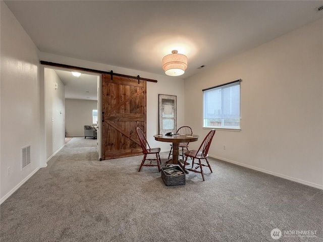 dining room featuring a barn door, baseboards, visible vents, and carpet flooring