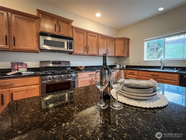 kitchen featuring dark stone countertops, brown cabinetry, appliances with stainless steel finishes, and a sink