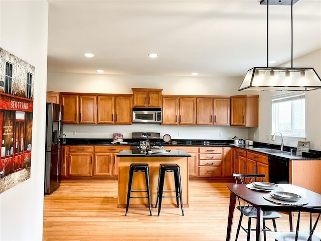 kitchen featuring brown cabinetry, a kitchen island, light wood-style flooring, a sink, and appliances with stainless steel finishes