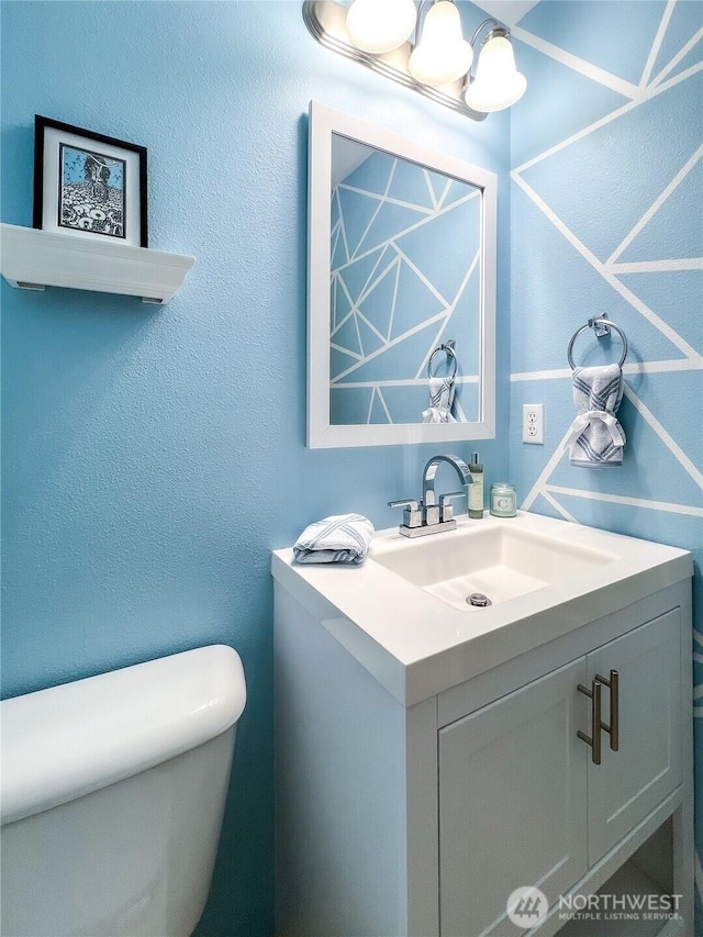 half bathroom with vanity, toilet, and a textured wall