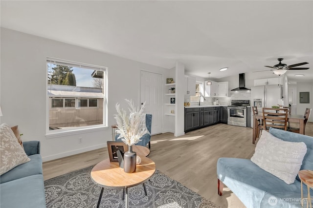 living area with a ceiling fan, baseboards, electric panel, and light wood finished floors