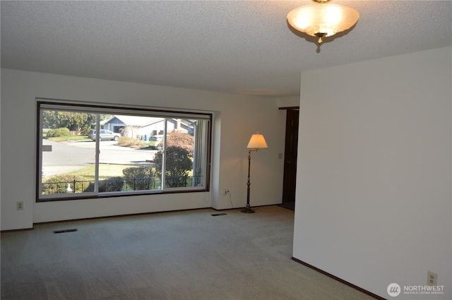 unfurnished room featuring a textured ceiling, carpet, visible vents, and baseboards