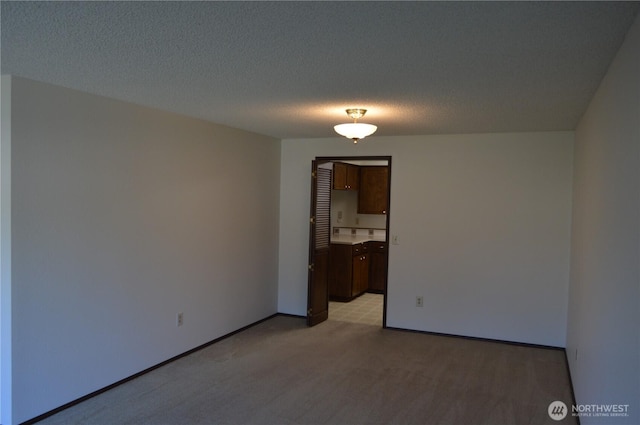 spare room featuring light carpet, a textured ceiling, and baseboards