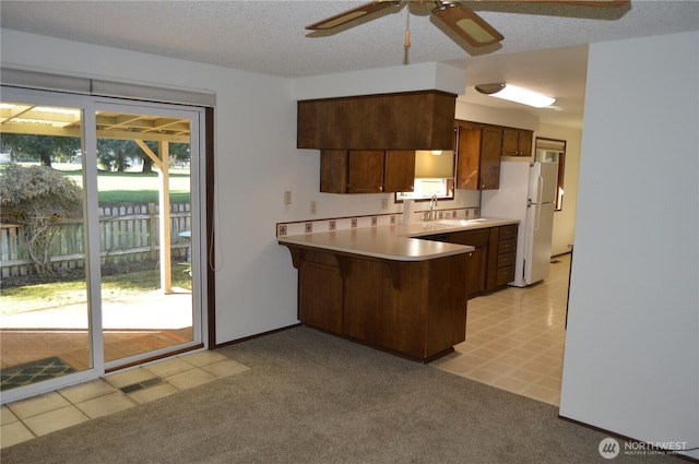 kitchen featuring light carpet, a peninsula, light countertops, and freestanding refrigerator