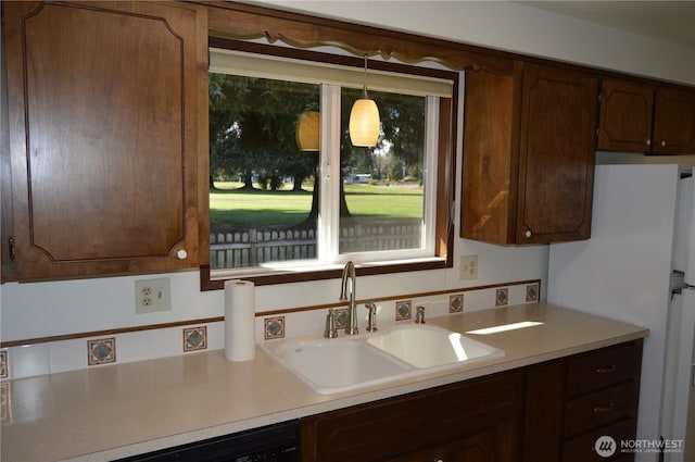 kitchen featuring light countertops, hanging light fixtures, freestanding refrigerator, a sink, and dark brown cabinetry